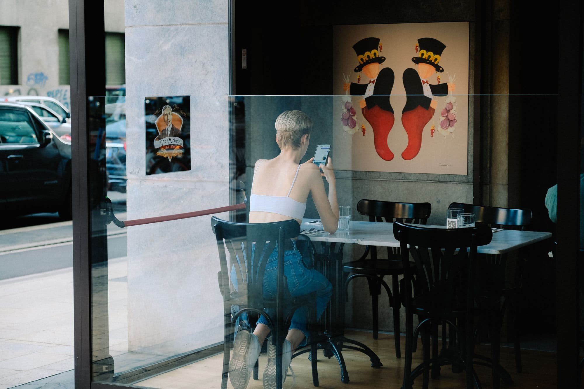 A woman using her phone at a café table, seen through the window