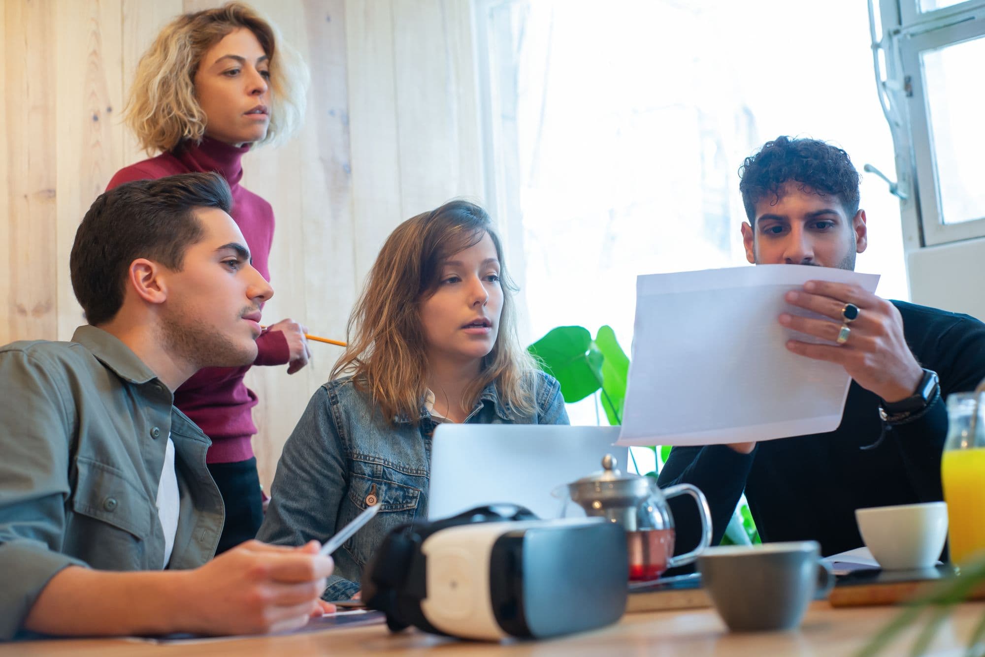 Four colleagues discussing a project around a table in a sunlit office