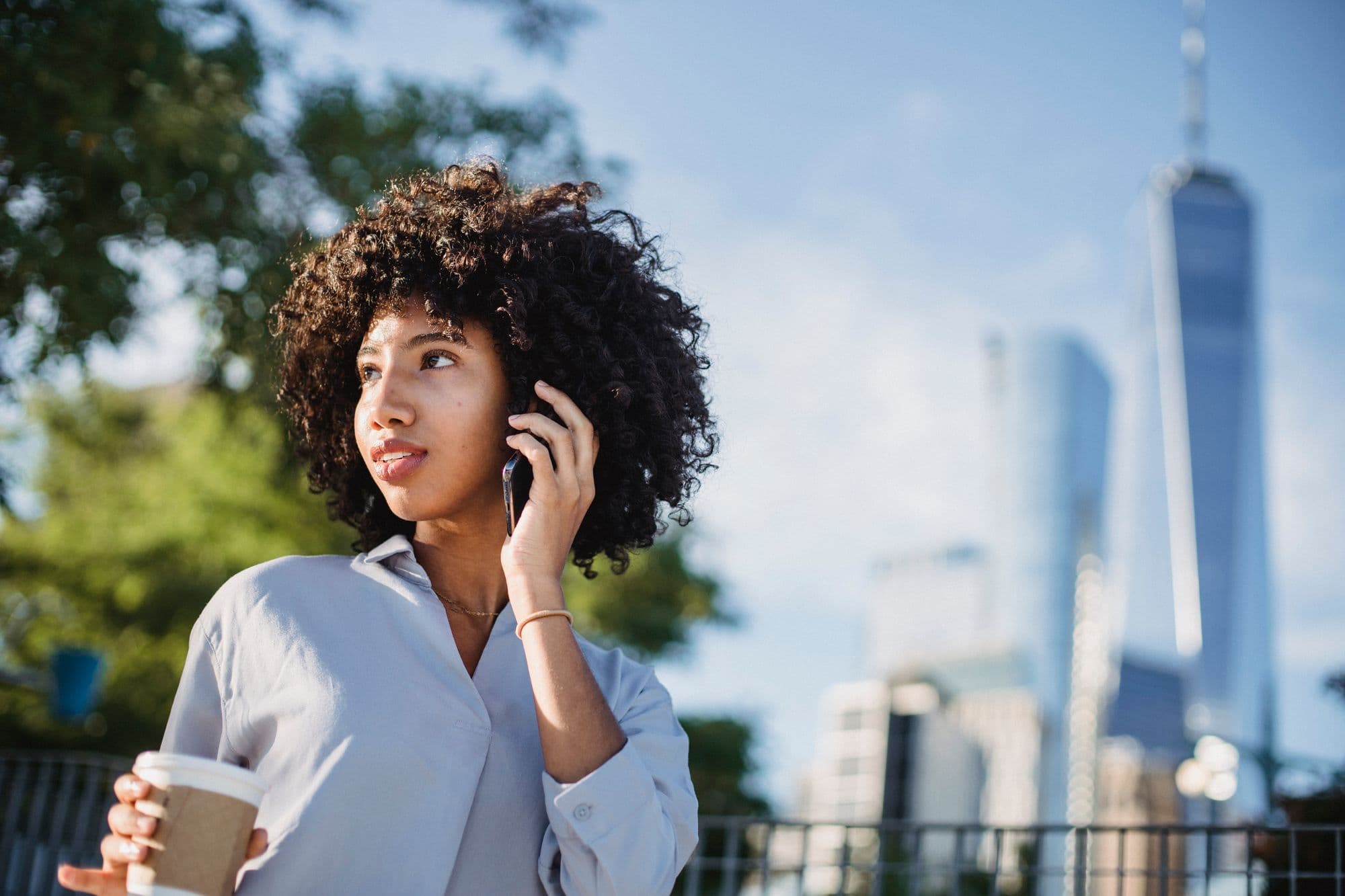A woman holding a coffee and talking on her phone outdoors in the city