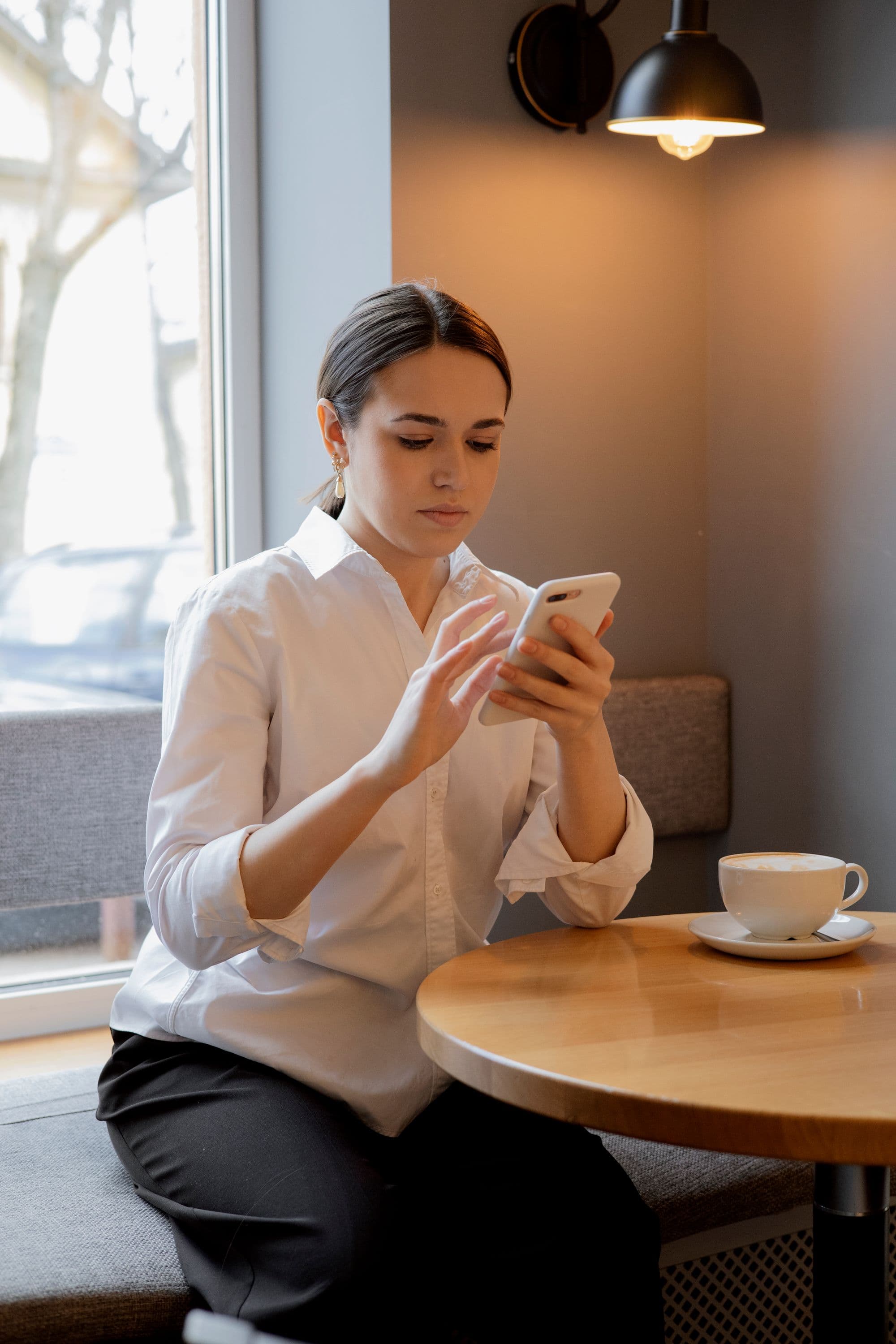 A woman checking her smartphone with coffee at a café table
