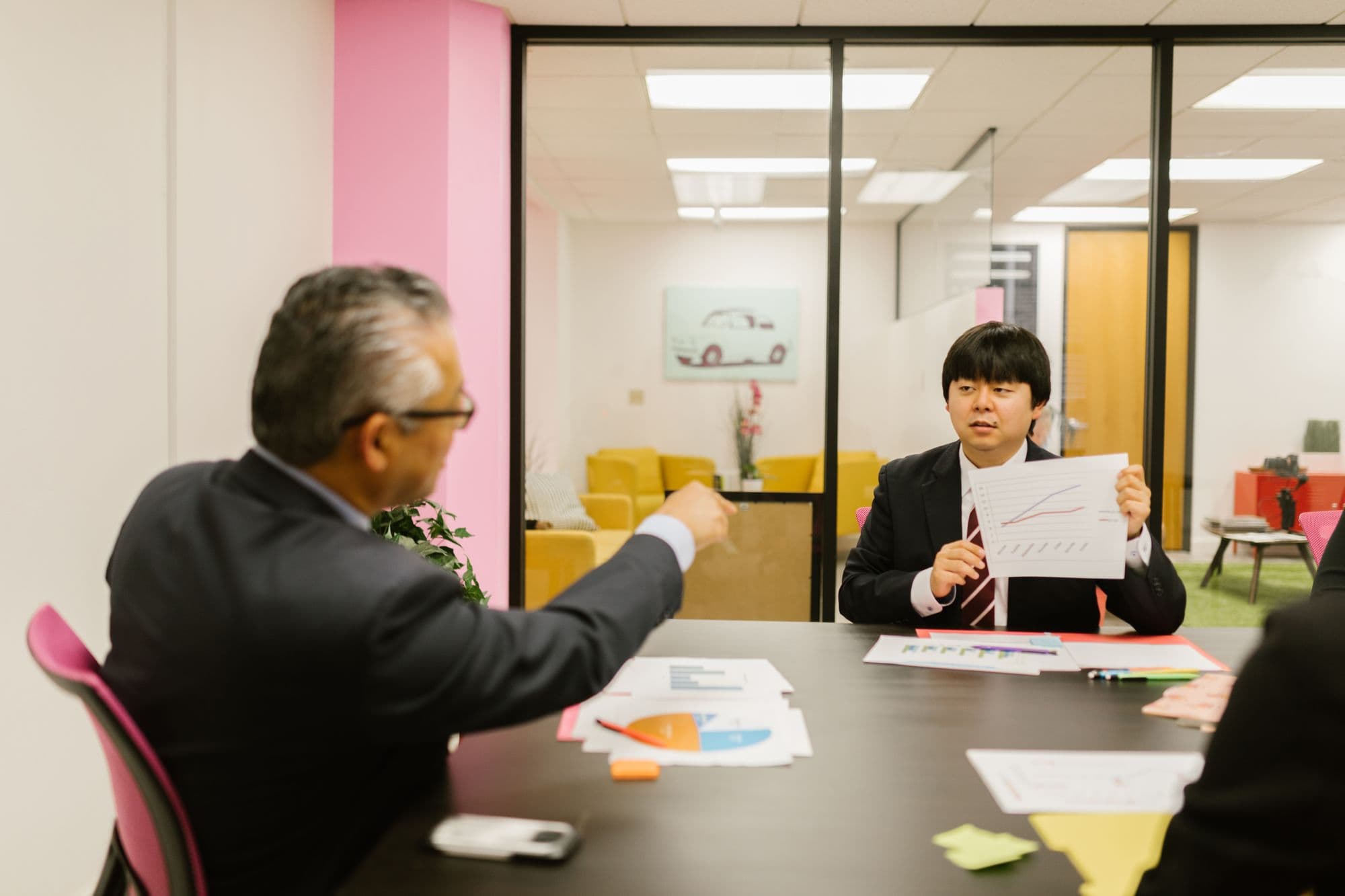 Two professionals reviewing data charts in an office with a pink wall