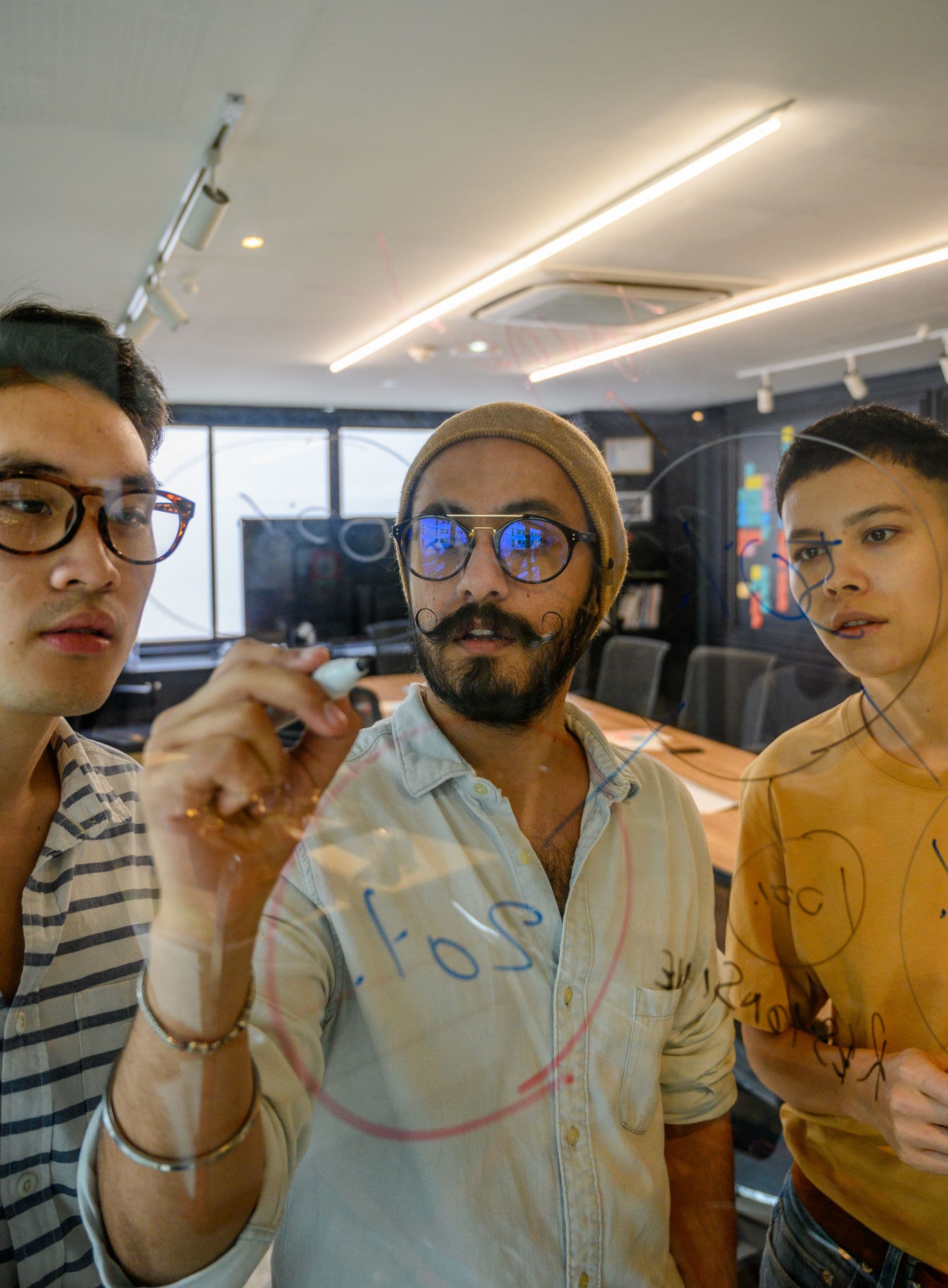 Three teammates sketching connections on a transparent board