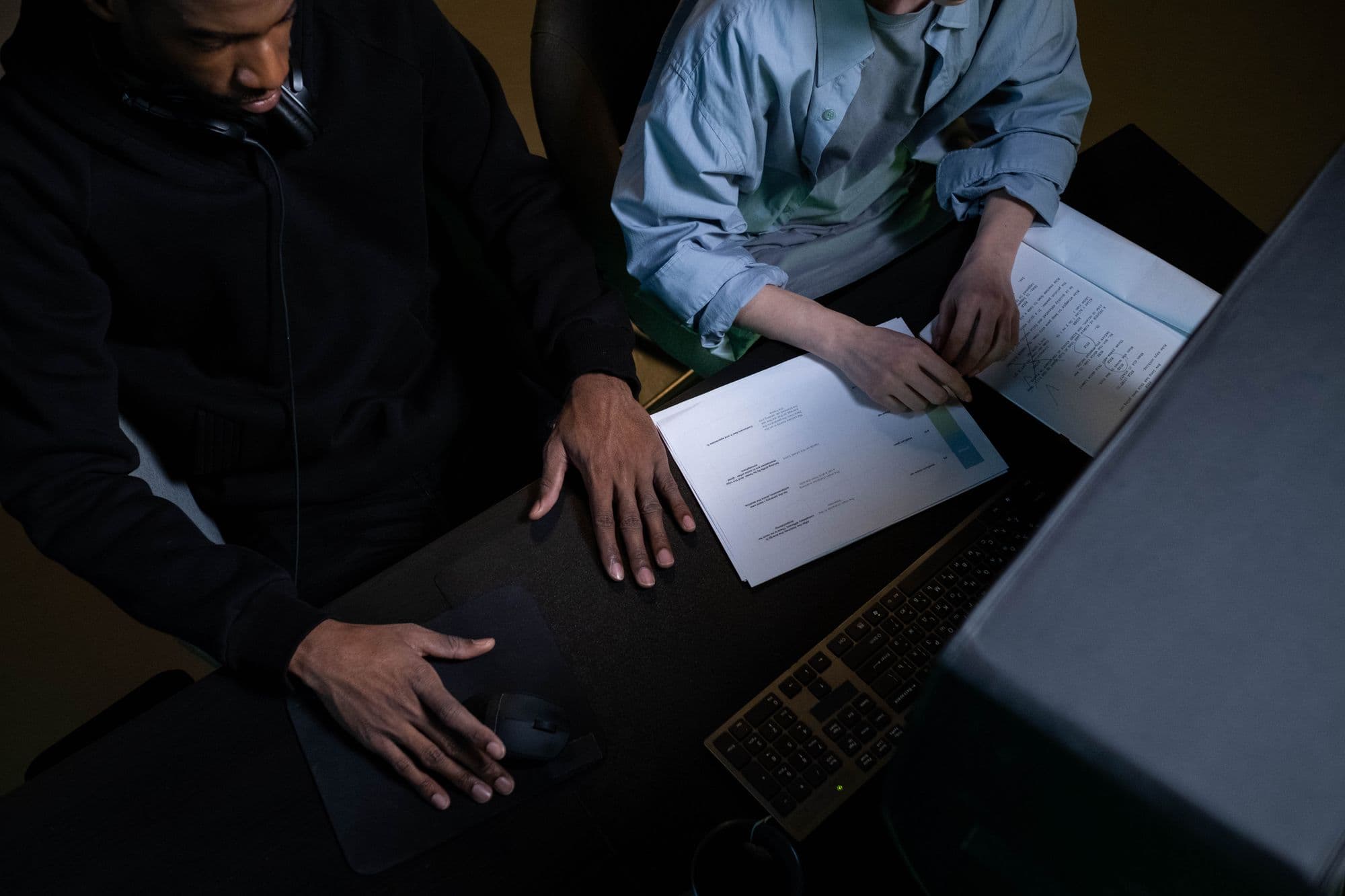 Two colleagues collaborating over papers and a computer at their desk